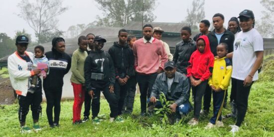 Group photo of about 15 people posing in a green field in front of some metal-roofed buildings.