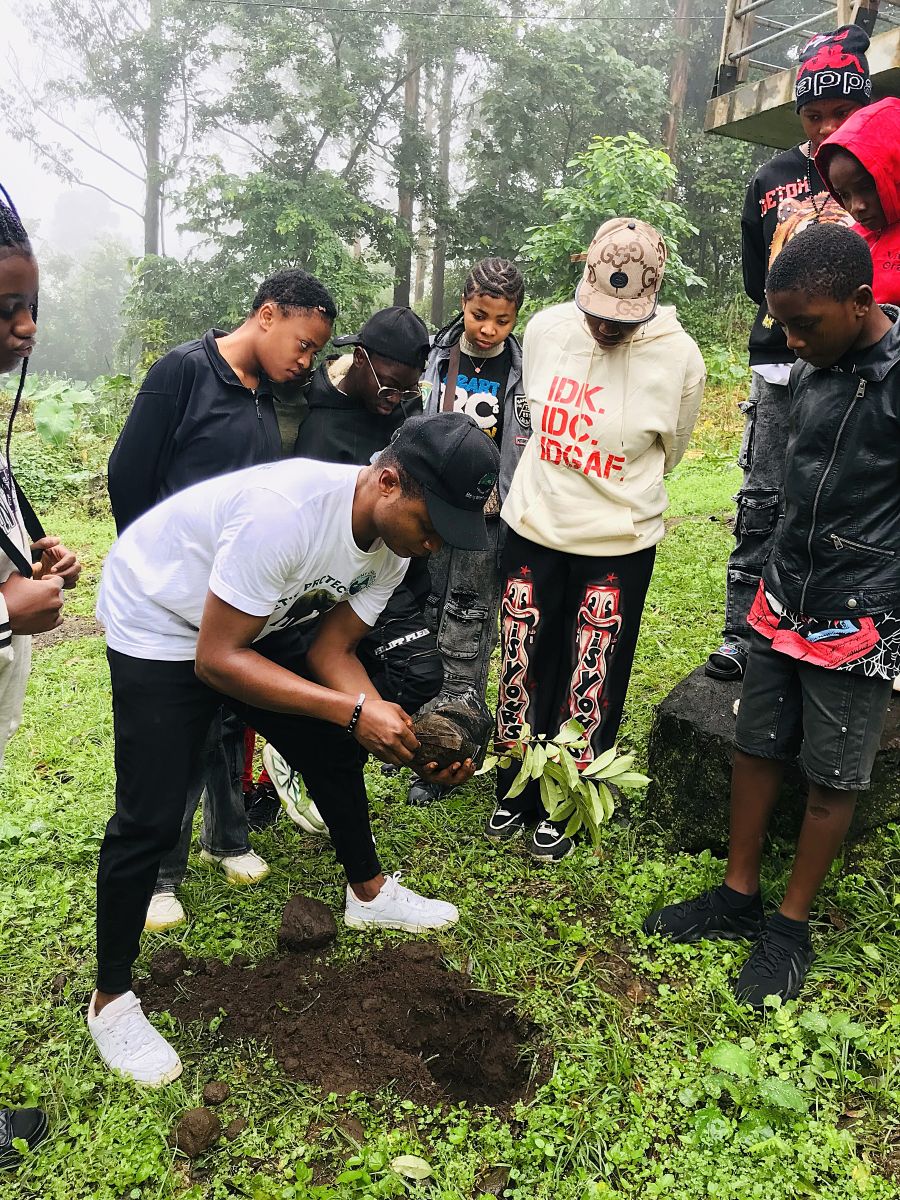 A man plants a small tree in a hole as a number of young people look on.