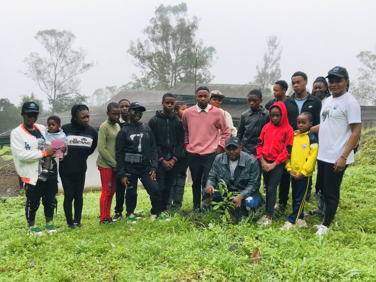 Group photo of about 15 people posing in a green field in front of some metal-roofed buildings.
