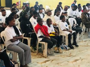 Many people seated in white chairs listening attentively to a speaker at World Elephant Day.
